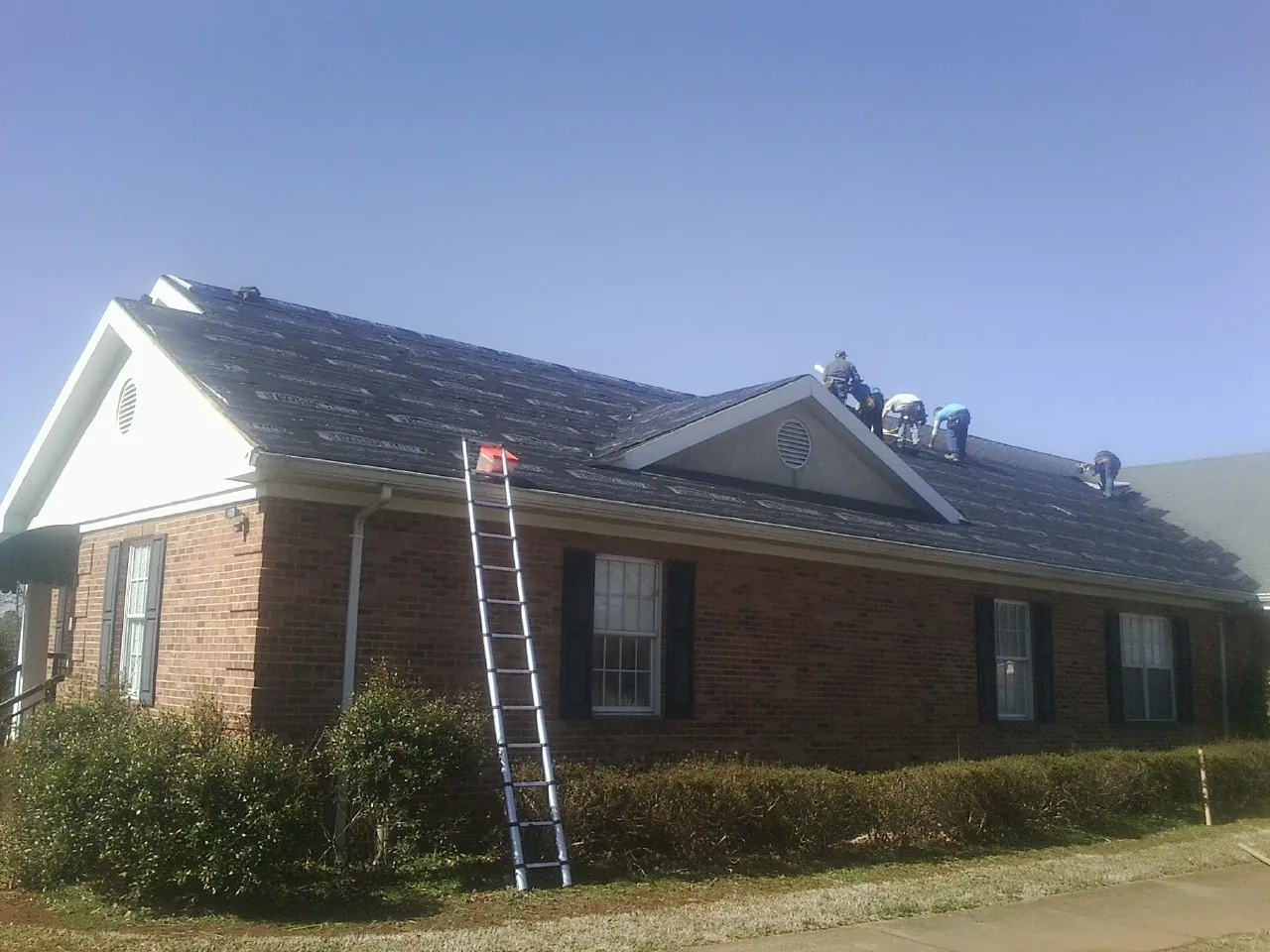Crew tearing shingles off a brick ranch roof with a ladder set — Emergency Roof Repair work by our crew in Sunol