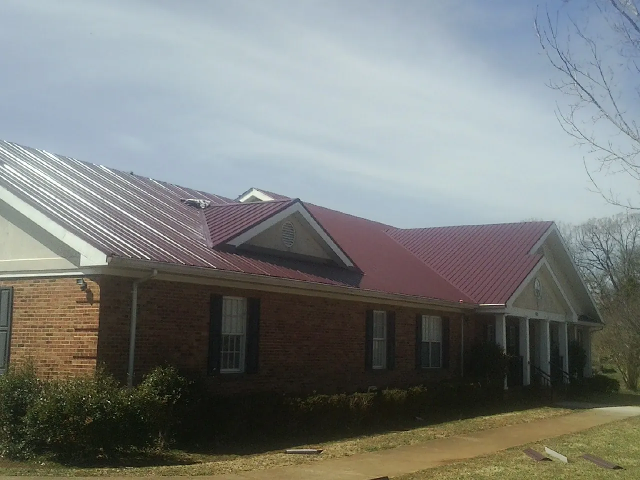 Red metal roof with gabled entries on a long brick building, from a Hail Damage Roof Repair job in Sunol