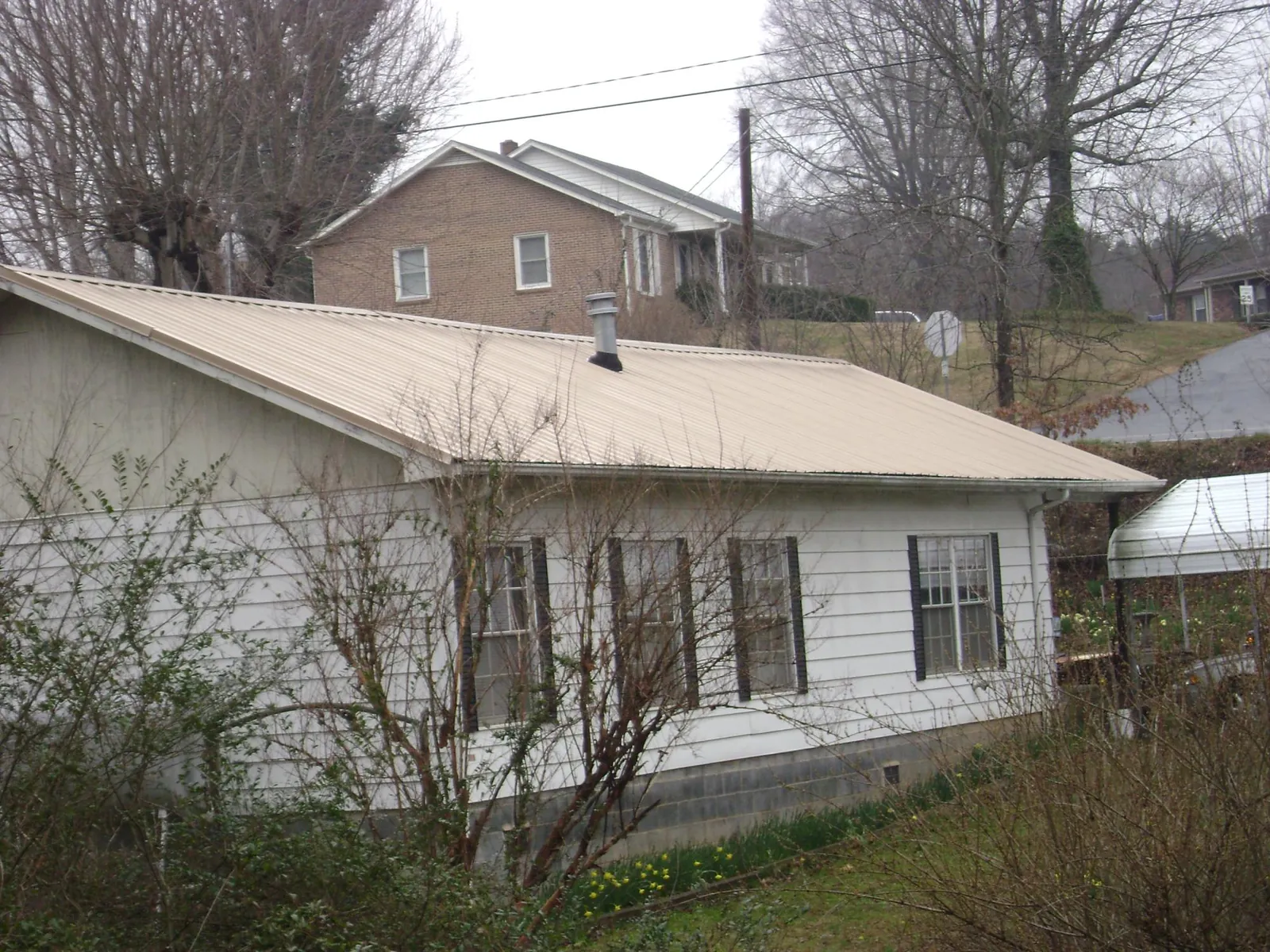 Tan metal roof on a white sided house set into a hillside — Commercial Roofing by Roofing Brothers in Sunol
